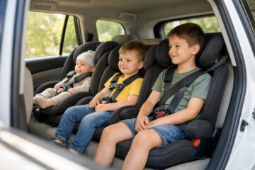 Tre bambini di età diversa seduti in tre seggiolini auto installati sul sedile posteriore di un’auto familiare