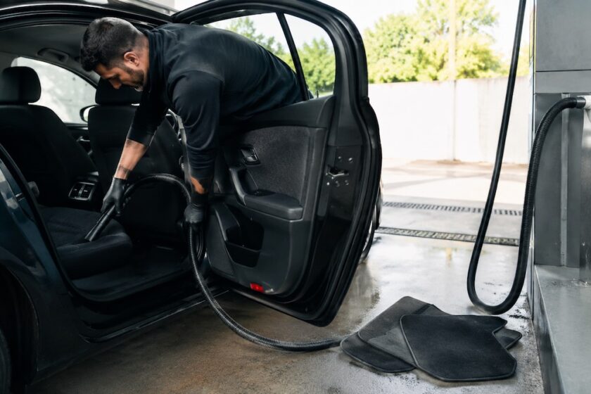 Persona pulisce gli interni dell’auto con aspiratore in un autolavaggio fai da te