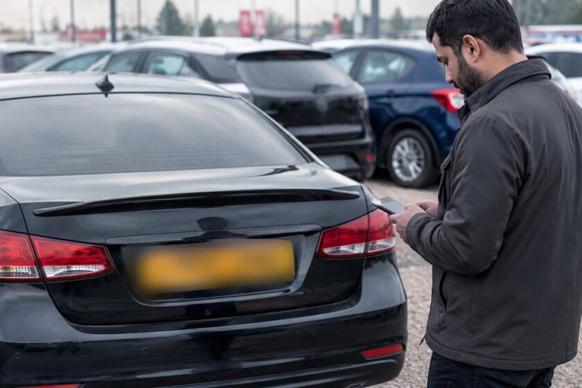 Persona con smartphone verifica la targa di un’auto usata prima dell’acquisto